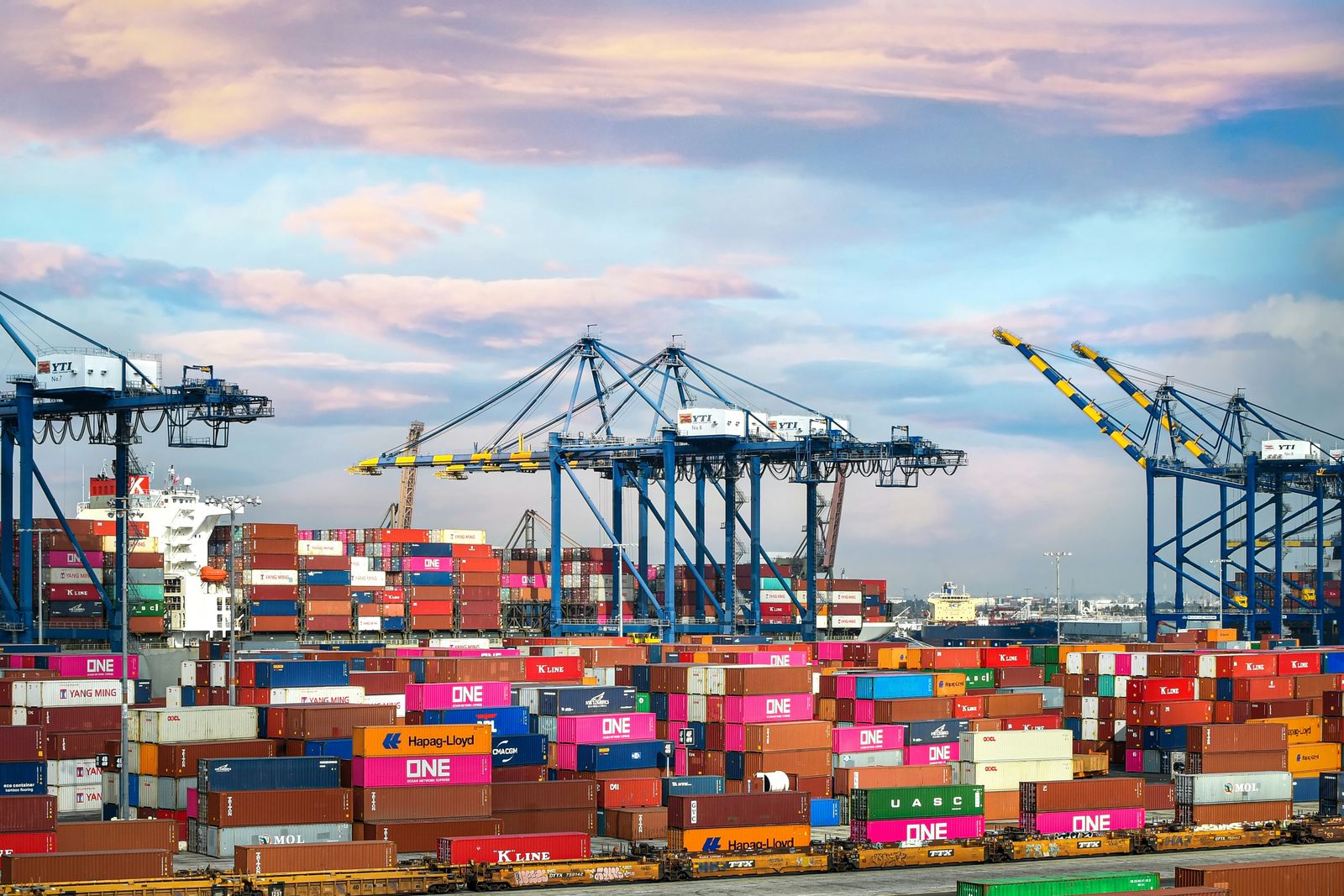 Shipping containers stacked at a port with cranes behind